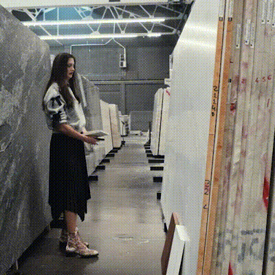 A woman stands in a warehouse surrounded by stacked boxes, indicating a busy storage environment.